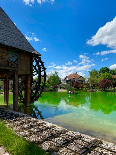 A vertical shot of a green lake with a house in the background on a sunny day