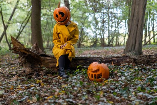 A closeup shot of a young woman wearing a pumpkin head in the forest