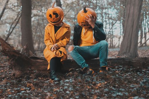 A closeup shot of a couple wearing pumpkin heads in the forest