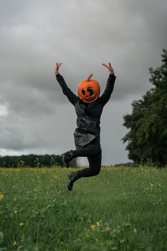 A vertical shot of a young woman wearing a pumpkin on her head in the forest