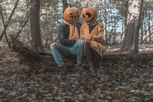 A closeup shot of a couple wearing pumpkin heads in the forest
