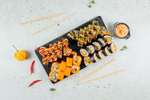 A top view of different types of sushi served on a granite board with sauce and chopsticks for two