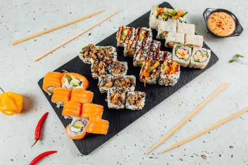 A top view of different types of sushi served on a granite board with sauce and chopsticks for two
