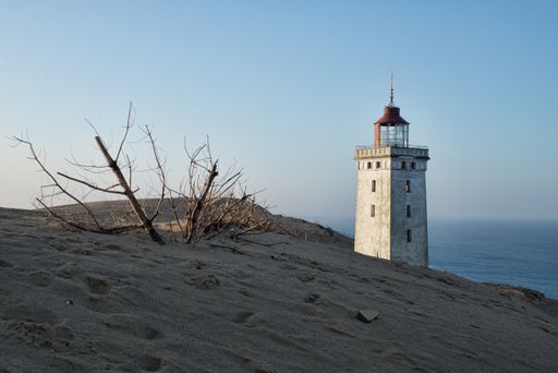 A low angle shot of a lighthouse standing on top of a hill during sunset