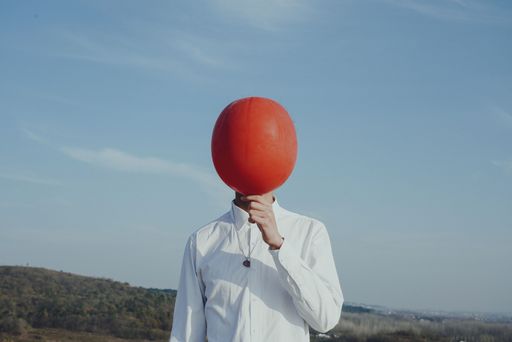 A person holding a red balloon in front of his face