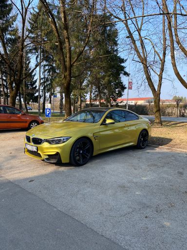 A vertical shot of a modern yellow BMW M4 parked in a parking lot
