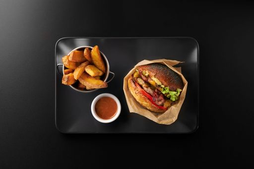 A top view of a burger near fried potato in a bucket on a black plate