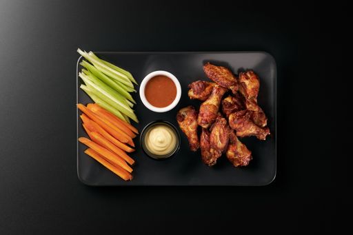 A top view of Chicken wings with sauces and cut vegetables