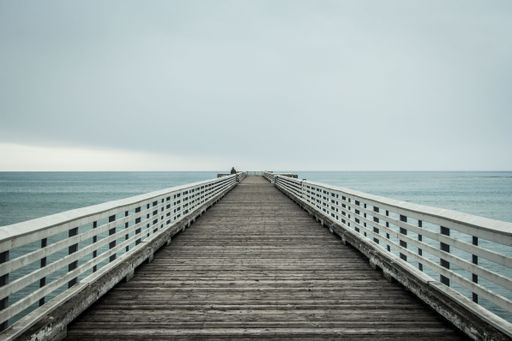 A scenic view of a fisherman looking out to the sea while standing on a wooden pier