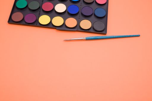 A closeup shot of a watercolor palette and a brush isolated on an orange background