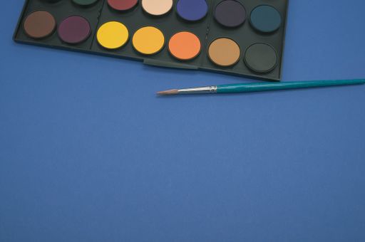 A closeup shot of a watercolor palette and a brush isolated on a blue background