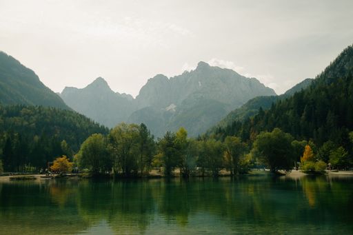 A scenic view of lake Jasna surrounded by trees and vegetation with a mountain in the background