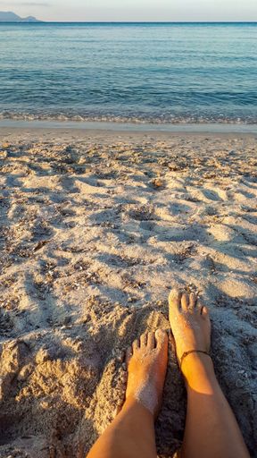 A vertical shot of a person's feet in the sand at the beach