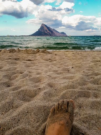 A vertical shot of a person's feet in the sand at a beach in Sardinia, Italy