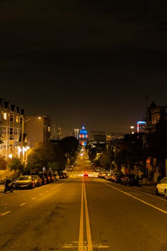 A vertical shot of a road with parked cars at night