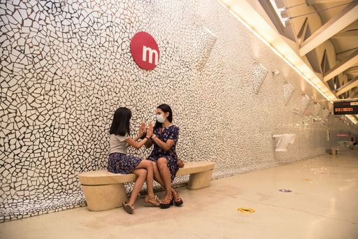 A young Hispanic mother and her daughter wearing medical masks and playing a game at the train station