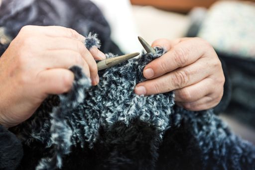 A closeup shot of female hands knitting with a fluffy fabric