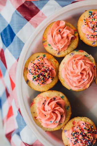 top down view of pink frosting with sprinkles on confetti birthday cupcakes in Tupperware