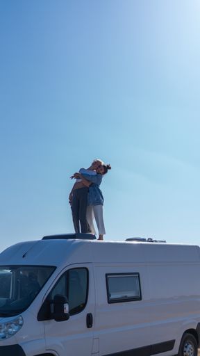 A vertical shot of two female friends smiling and hugging on top of a bus during a road trip