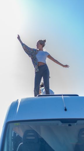 A vertical shot of a young female posing on top of a white bus