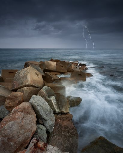 A vertical shot of rocks in the sea during a thunderstorm and lightning