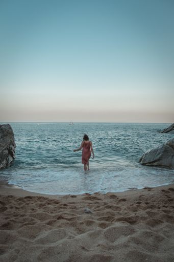 A vertical shot of a female walking in the sea surrounded by rocks in the evening
