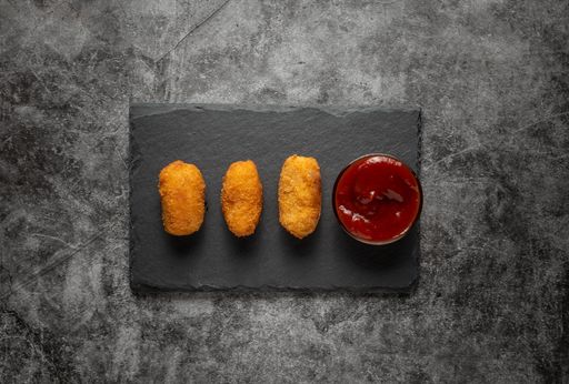 A top view of three croquettes served with a red sauce on a black board