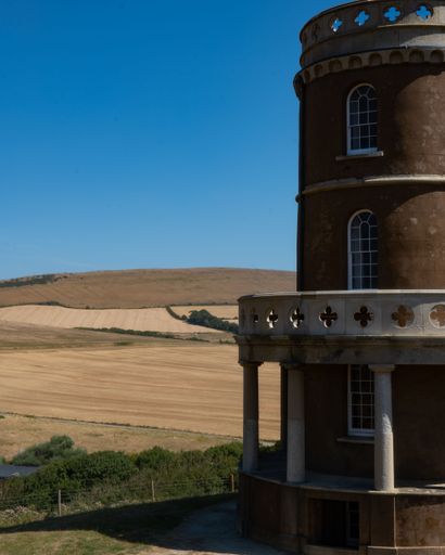 A beautiful vertical shot of the Clavell Tower in Kimmeridge, England with hills around it under a bright sky