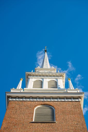 A low angle of brick and white steeple in the city of Boston against the blue sky