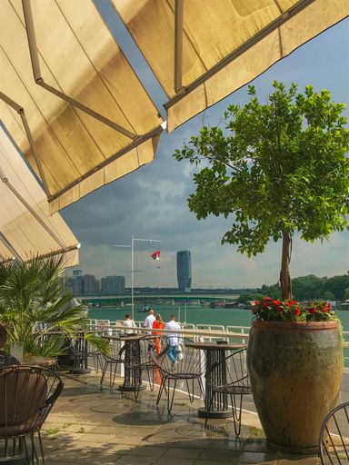 A vertical shot of an outdoor cafe with a view to the city buildings and a river in cloudy weather