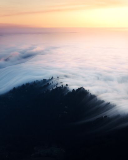 A mesmerizing shot of clouds covering the peaks of tree-covered mountains