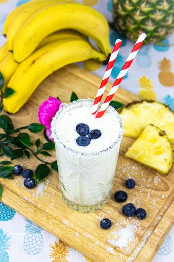A vertical top view of an iced drink with blueberries on it with  bananas ananas on the board