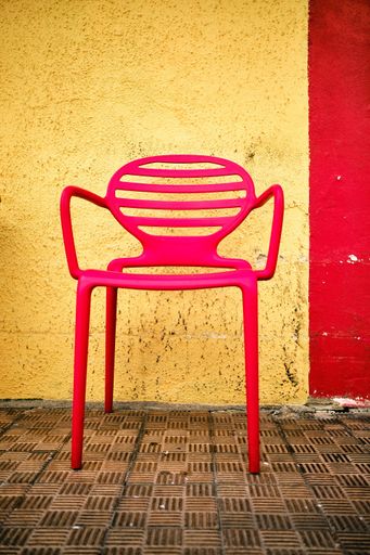 A vertical shot of a red chair in front of a yellow and red wall captured in Menton, French Riviera