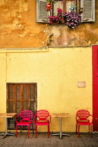 A vertical shot of a yellow wall wish chairs and tables on the pavement in Menton, French Riviera