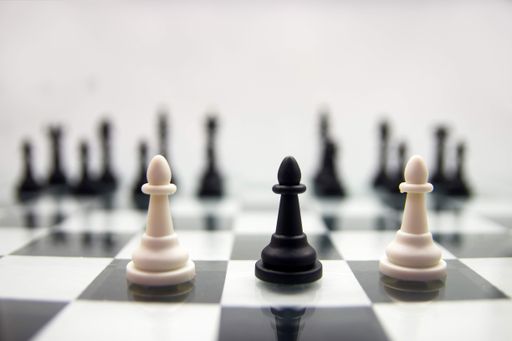 A Selective focus on two white and one black pawn chess piece on a chessboard set.