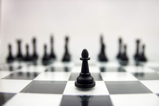 A closeup of a black pawn on a glossy chessboard on the blurry background of black chess pieces