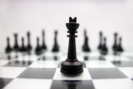 A close up of a black king chess piece on a glossy chessboard on the blurry background of its army