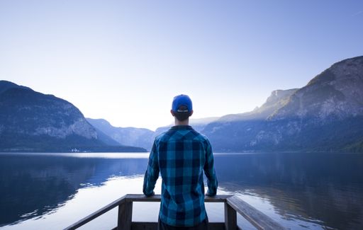A beautiful shot of a male standing on the pier in the lake surrounded by mountains and admiring the horizon