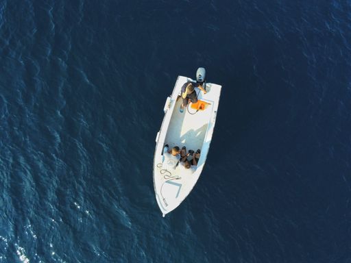 An aerial top view of two people on a boat sailing on blue water