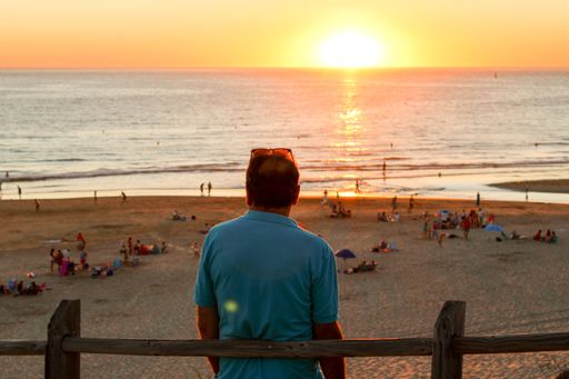 A back view of a male leaning on a wooden fence and looking at the beautiful sunset reflecting on the sea