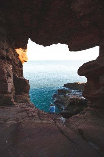 A vertical shot of a female sitting on the rock above the ocean taken from a hole on the rock