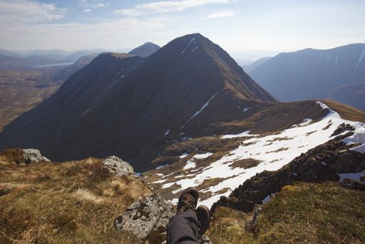 A high angle shot of the legs of a human sitting on the ground at the top of the mountains