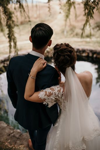 A vertical shot of the groom and bride embracing at the shore of a lake