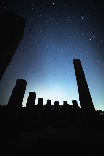 A vertical shot of stone formation silhouettes under a bright blue starry sky