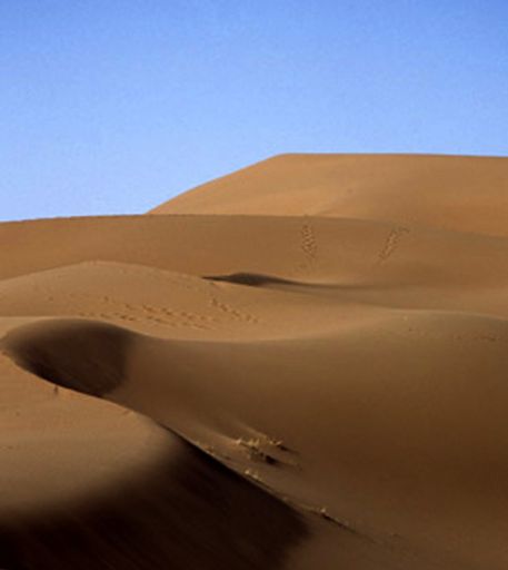 A vertical shot sandy hills in a desert with human traces and the sky in the background