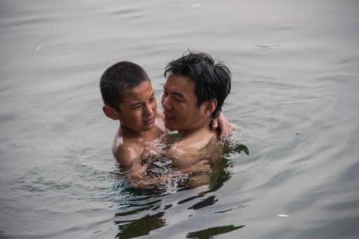 A father teaches his son to swim and comfort him in a lake of a public park in Beijing,China