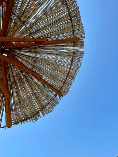 A vertical shot of a beach straw umbrella against a blue sky