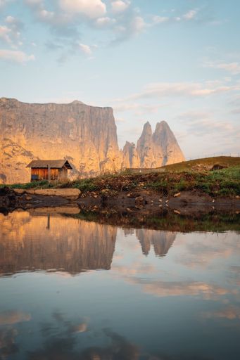 An old wooden hut and rocky mountains of South Tyrol reflected on a lake during the sunset