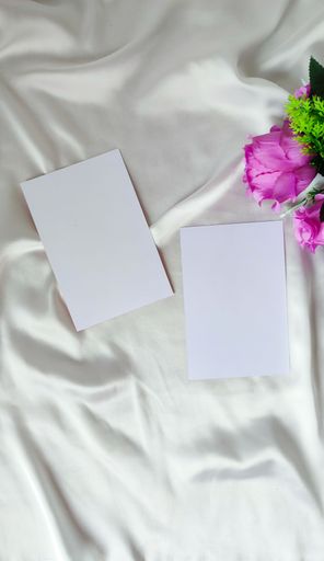 Two blank papers on a white cloth surface, purple flowers as a symbol of love and romance