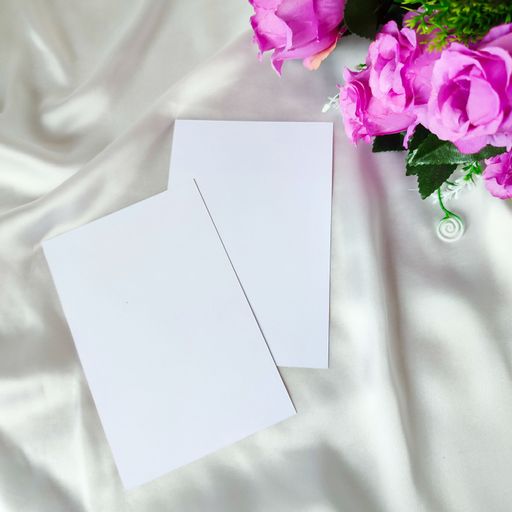 Two blank sheets of paper and decorative flowers on a white surface